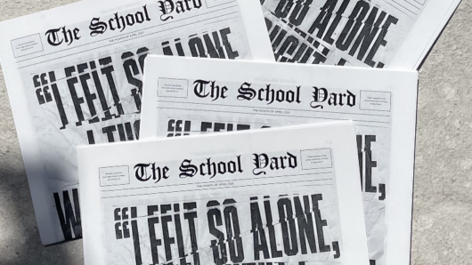 A photo of some news papers spread on concrete. The title says: The School Yard.