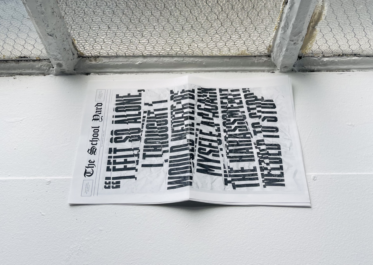 A photo of some news papers spread on concrete, near a fence wall. The title says: The School Yard.