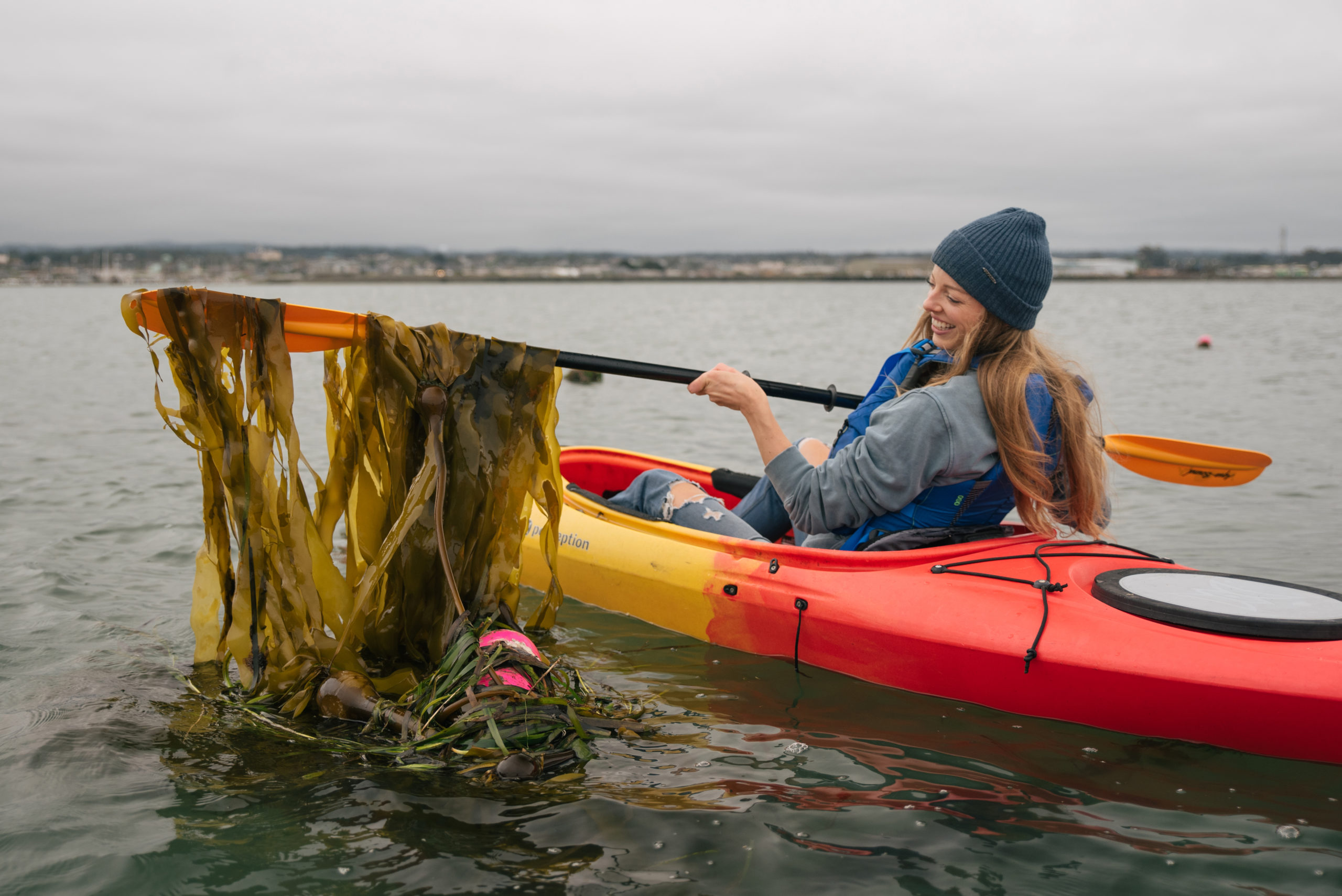 woman inside in a kayak showing seaweed in the boat paddle inside water