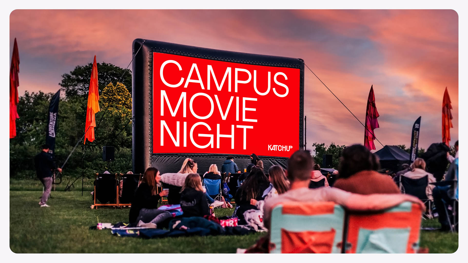 people sitting on the grass, with a temporary movie screen in front of them