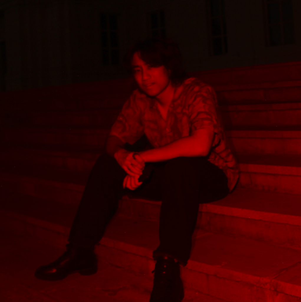 black and red image of man looking at camera while sitting on steps