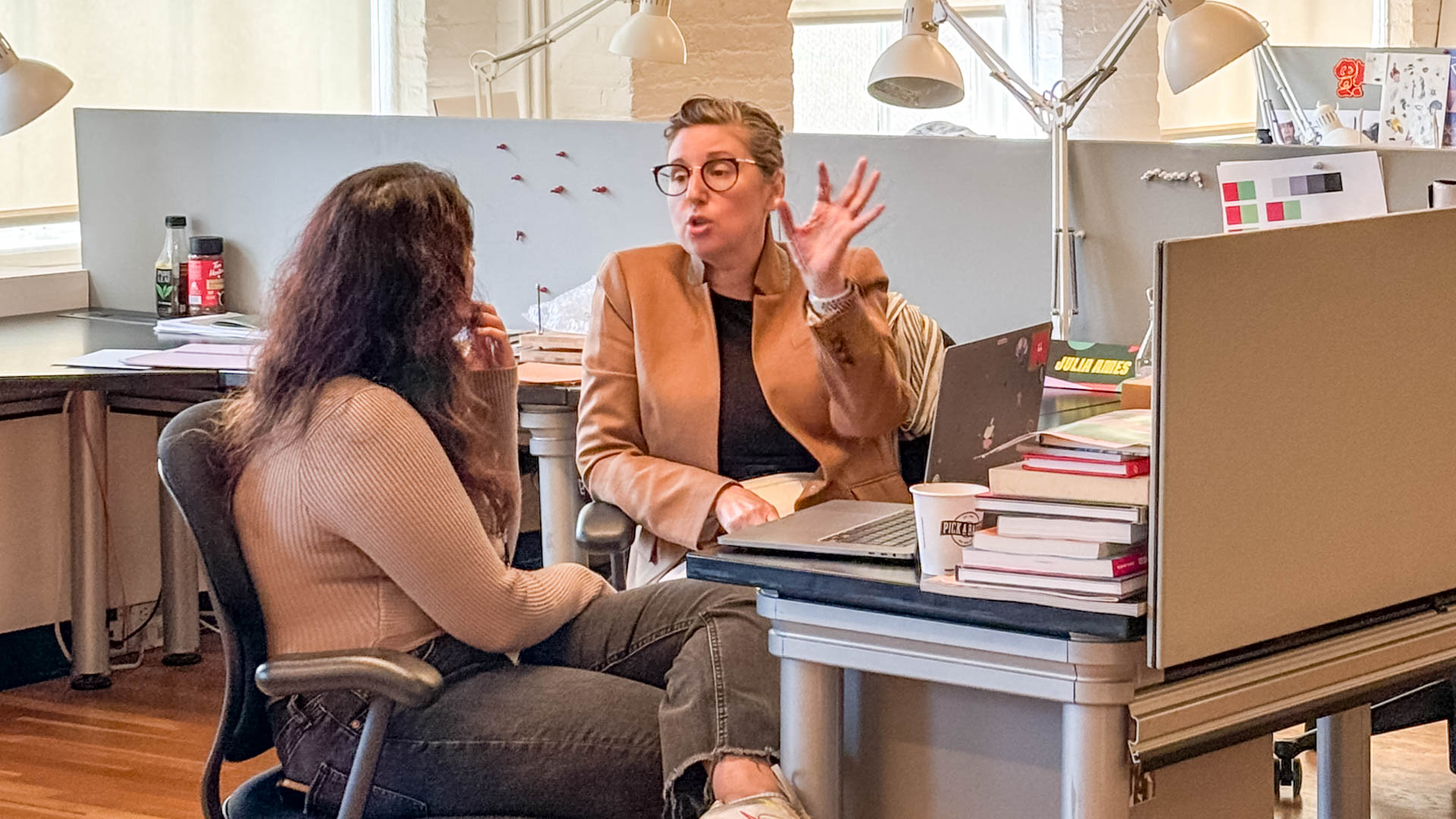 two people talking at a desk with a laptop computer