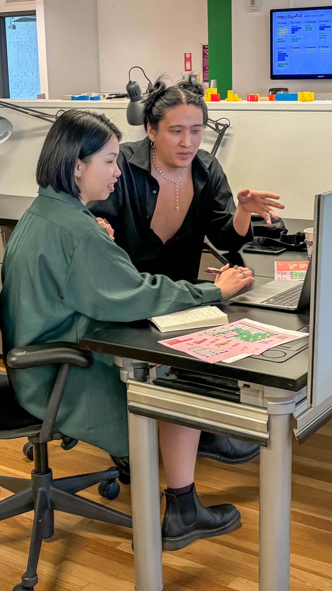 two people talking at a desk with a laptop computer