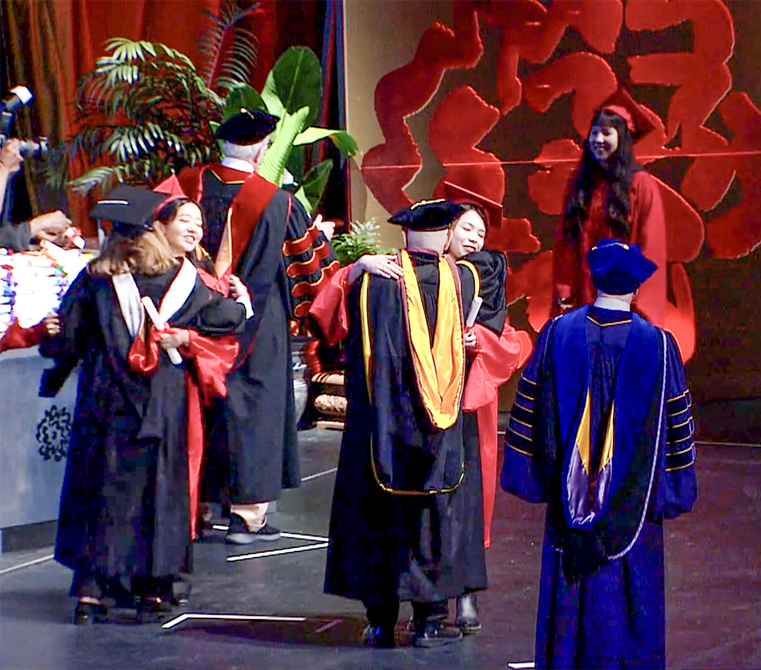 students on stage hugging professors at graduation