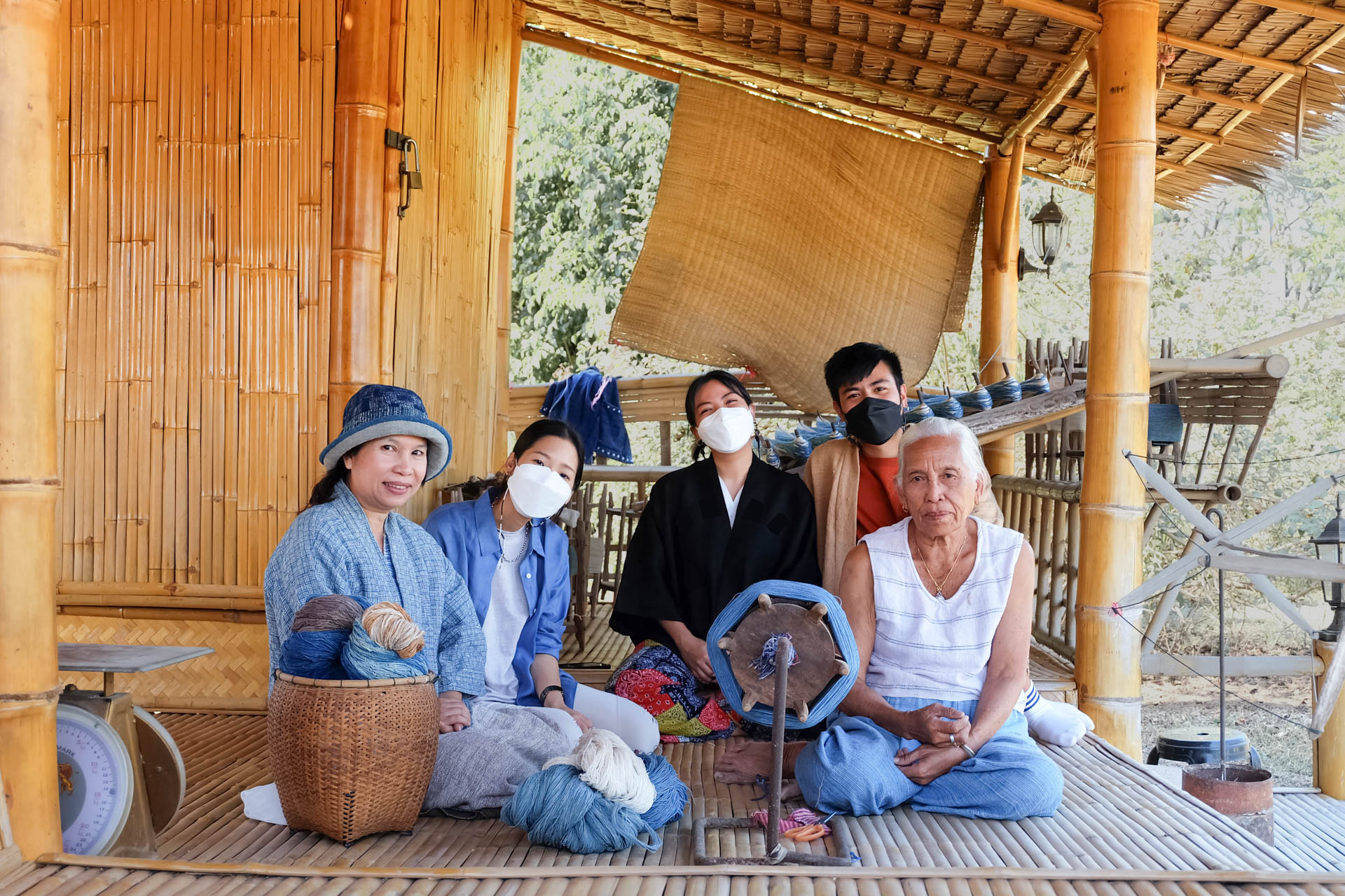 a group of Thai people sitting down on a porch with textile making machinery