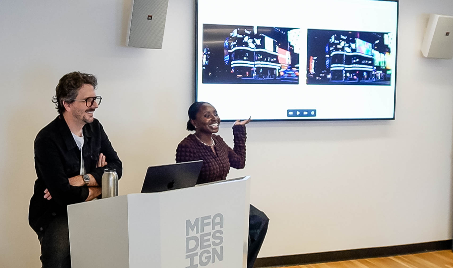 two people at a podium giving a lecture in front of a monitor