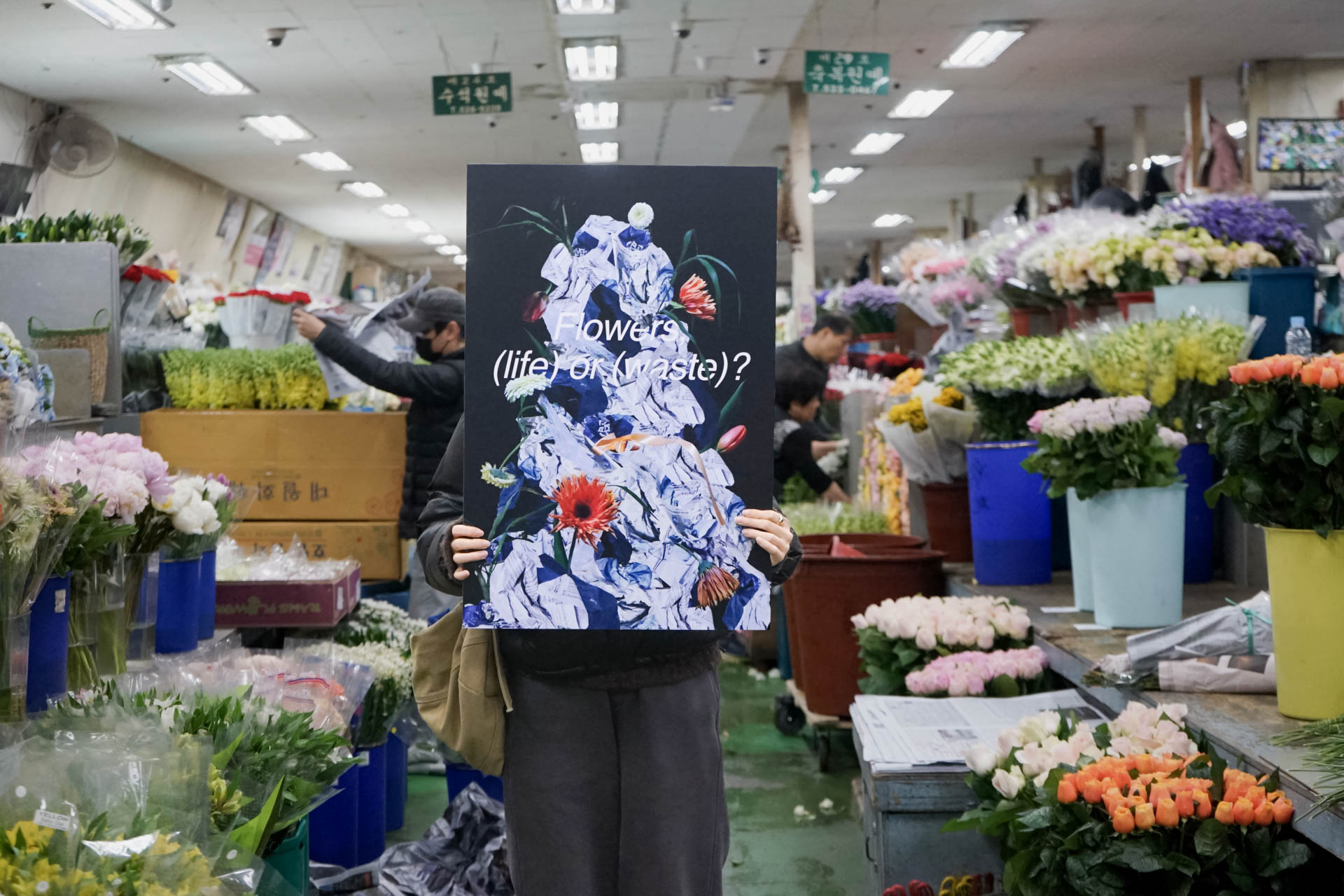 a crowded flower shop with a person holding a sign