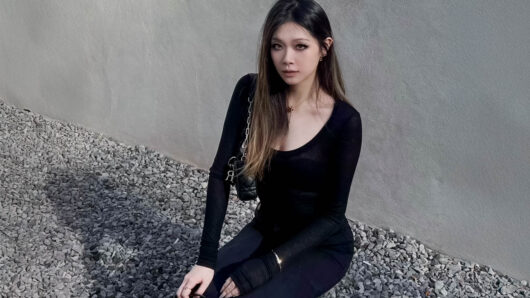 a woman with long hair looking at the camera, cement wall behind