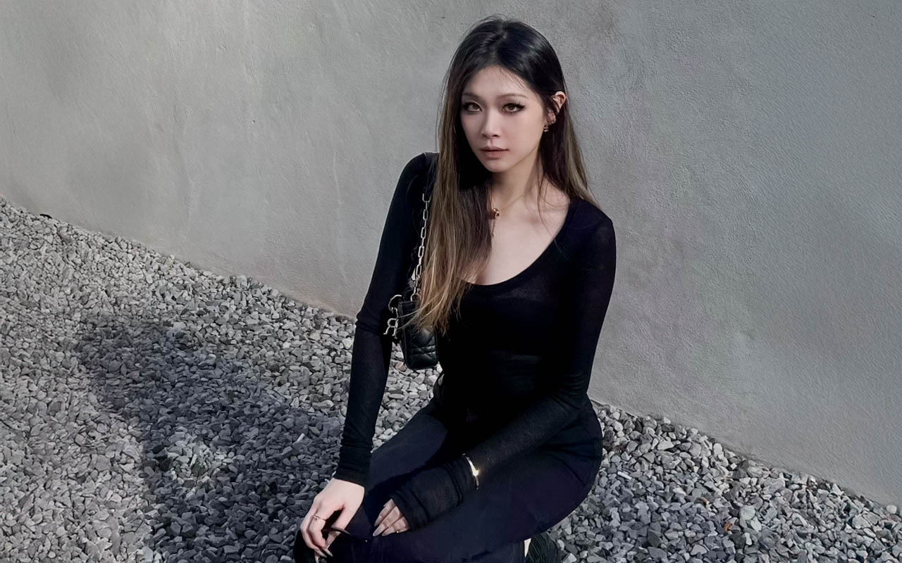 a woman with long hair looking at the camera, cement wall behind