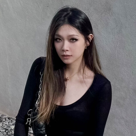 a woman with long hair looking at the camera, cement wall behind