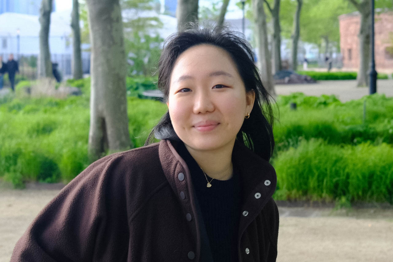 a woman looking at the camera with a park in the background