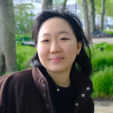 a woman looking at the camera with a park in the background