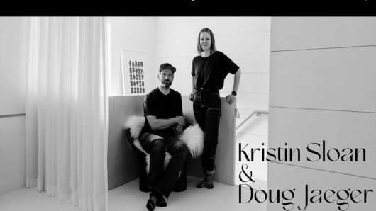 a man is sitting and woman is standing in a nice white room