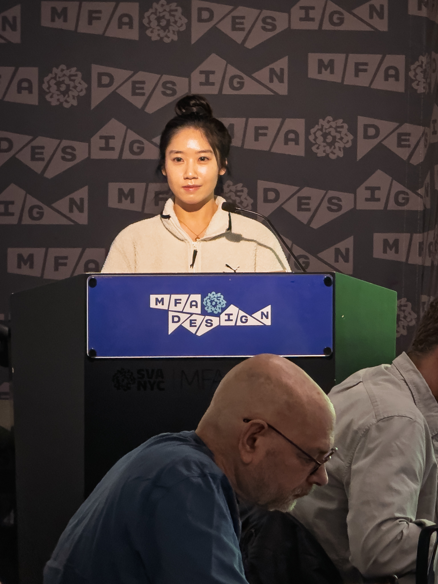 Woman at a podium with microphone, delivering a slide presentation
