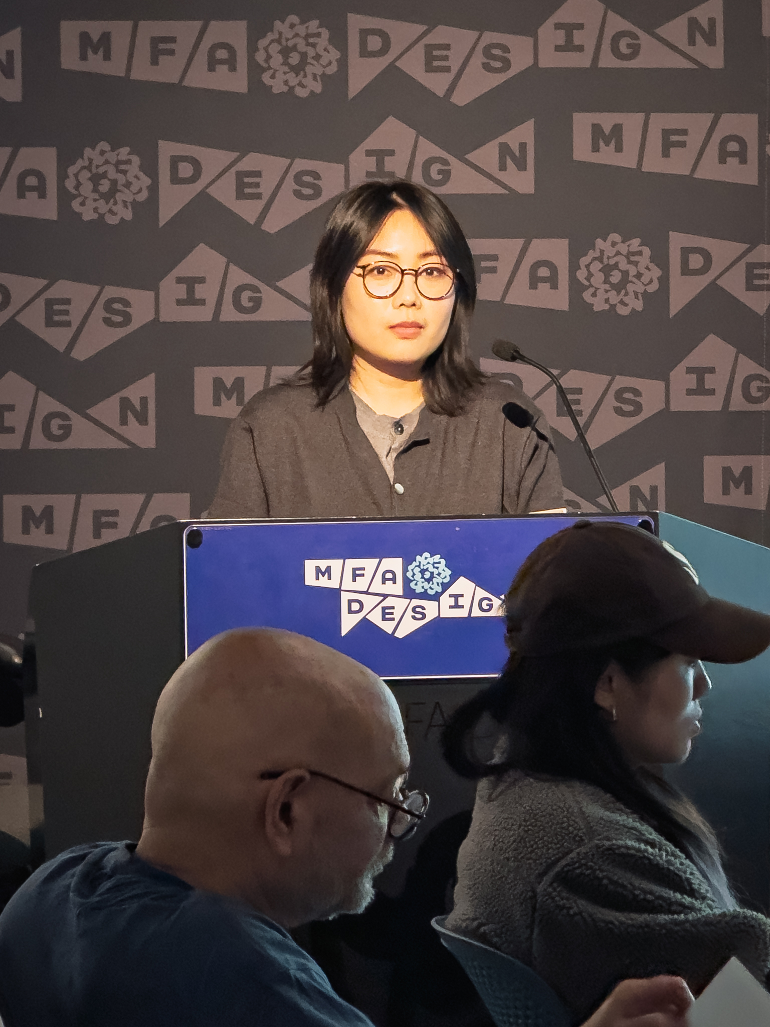 Woman at a podium with microphone, delivering a slide presentation
