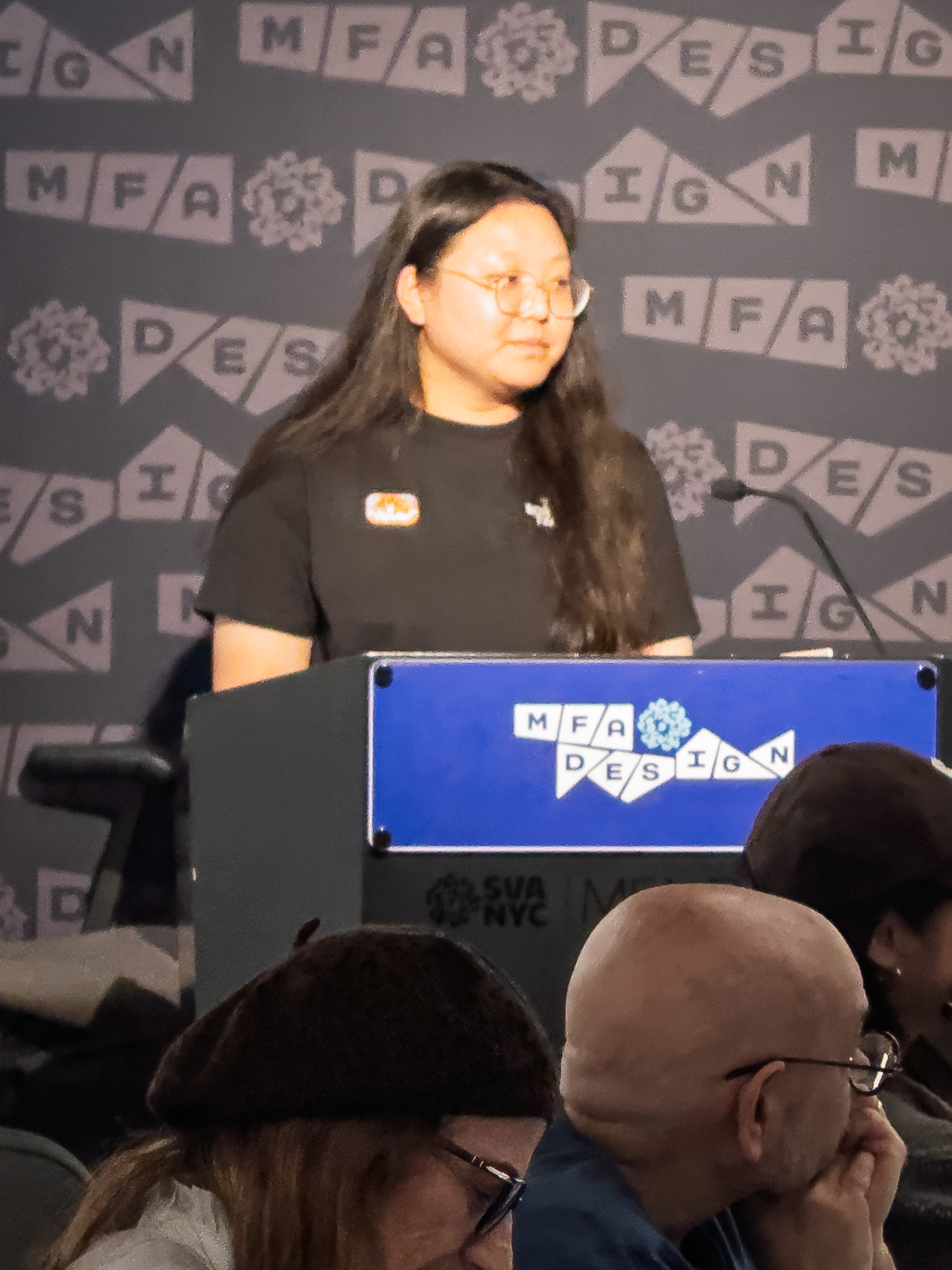 Woman at a podium with microphone, delivering a slide presentation