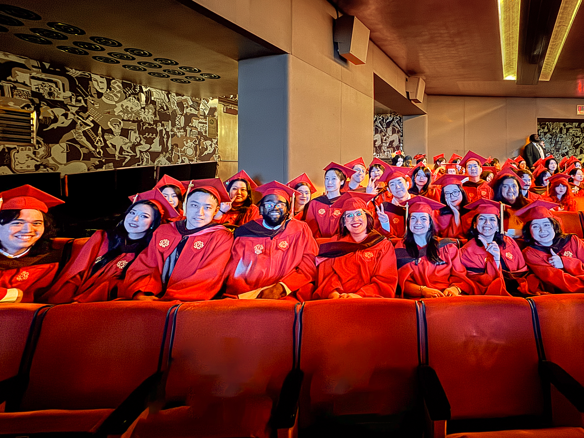 a group of students sitting in theatre seats in commencement gowns