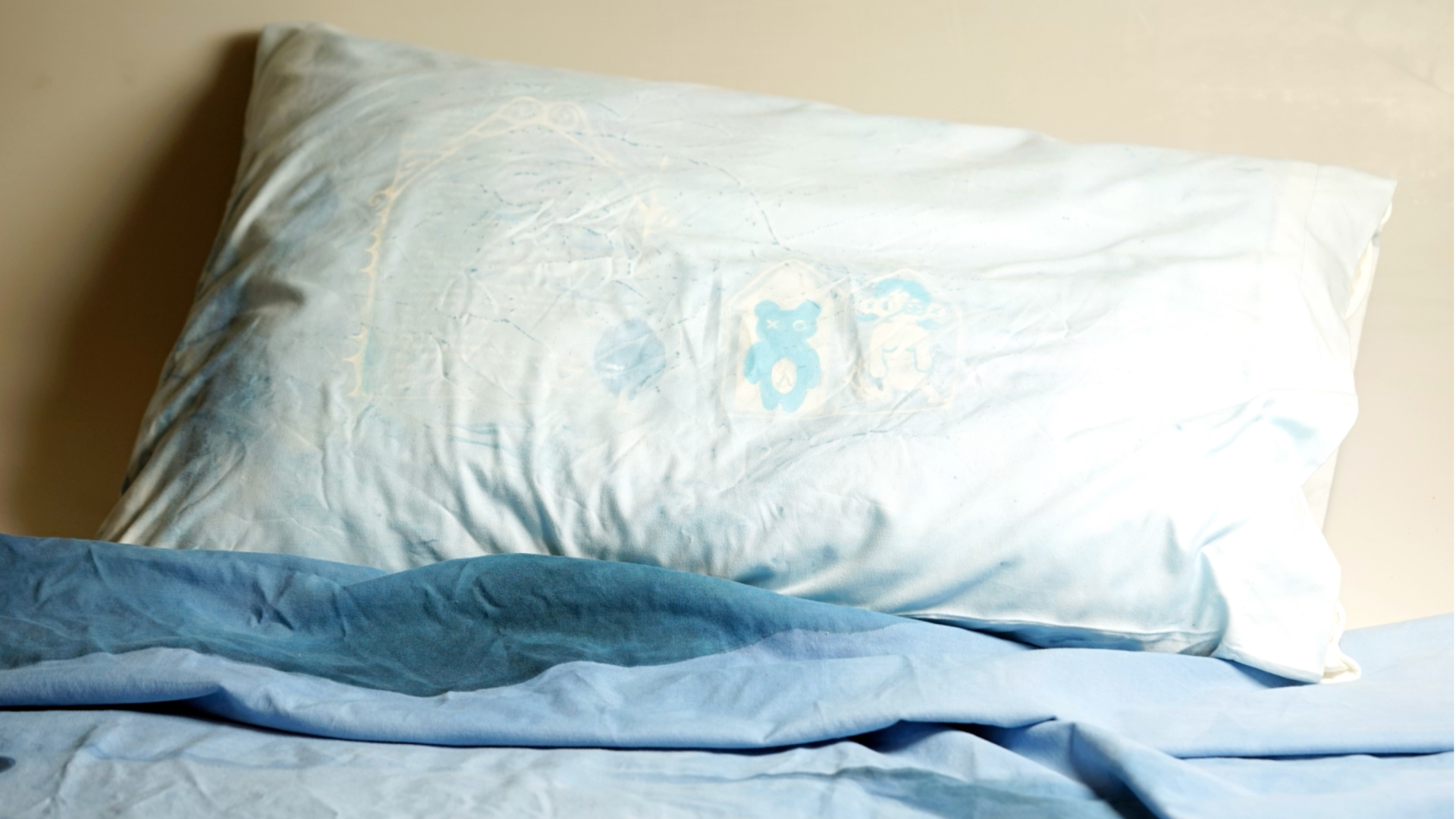 a white pillow on a bed with a blue comforter.
