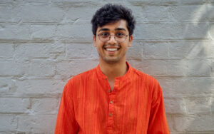portrait of a smiling man with glasses. White brick wall in background