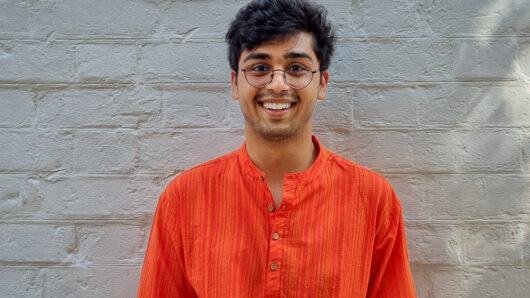portrait of a smiling man with glasses. White brick wall in background