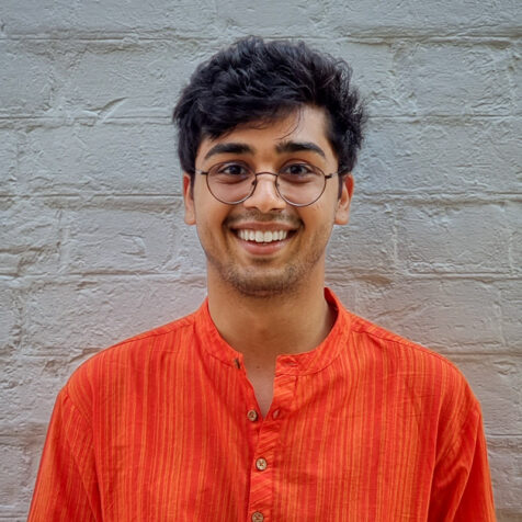 portrait of a smiling man with glasses. White brick wall in background