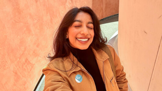 woman with long hair, nose ring and eyes closed smiles at the camera