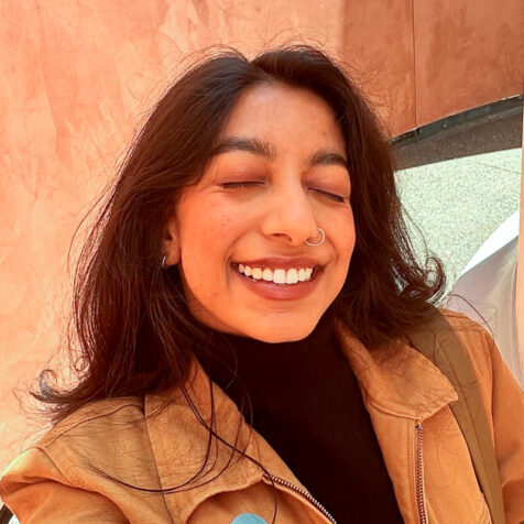 woman with long hair, eyes closed and a nose ring smiles at the camera