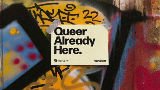 Street poster reading “Queer Already Here.” taped onto a graffiti-covered wall with Tandem branding.