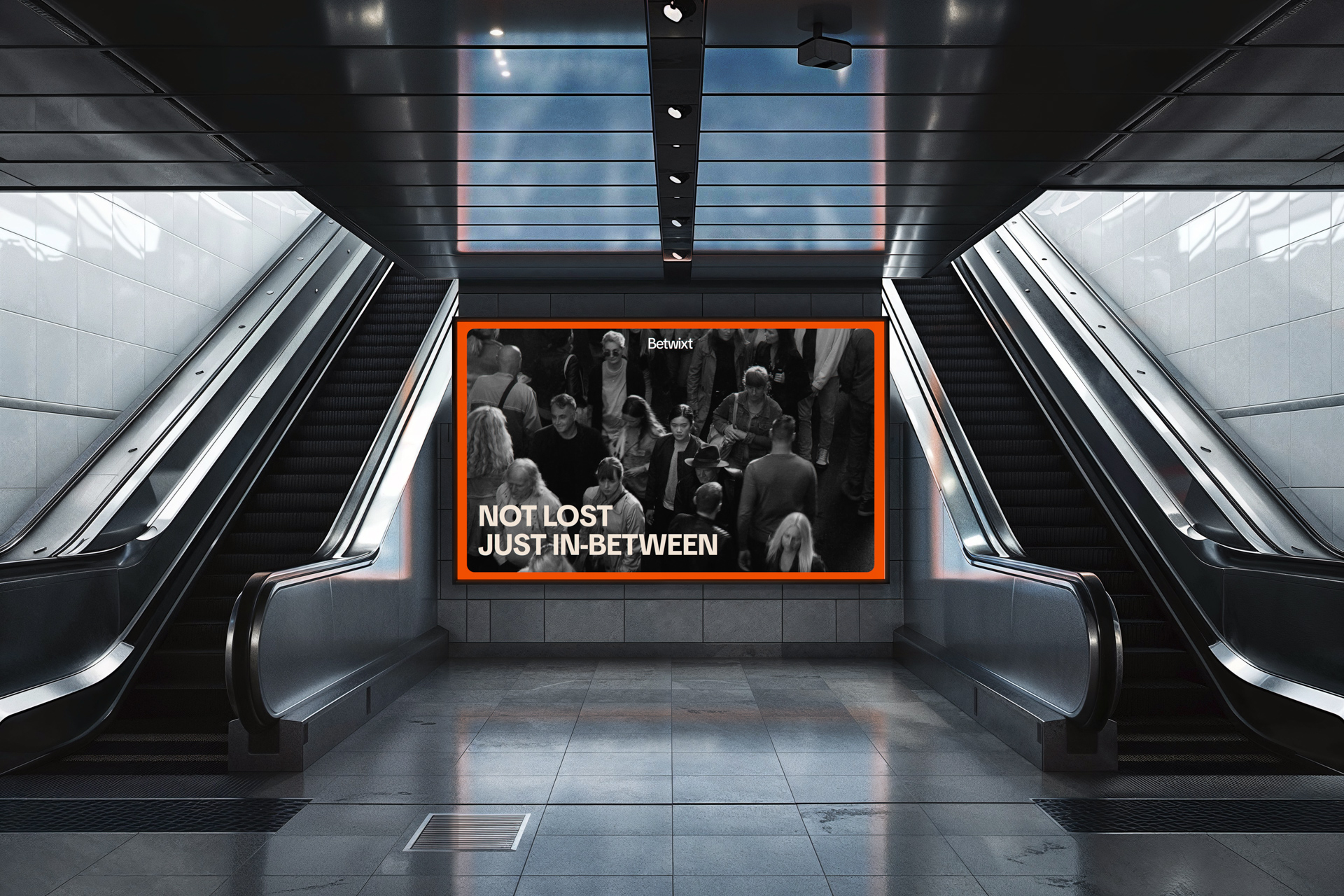 Modern subway station with escalators framing a digital billboard that reads “NOT LOST JUST IN-BETWEEN” above a crowded black-and-white city scene.
