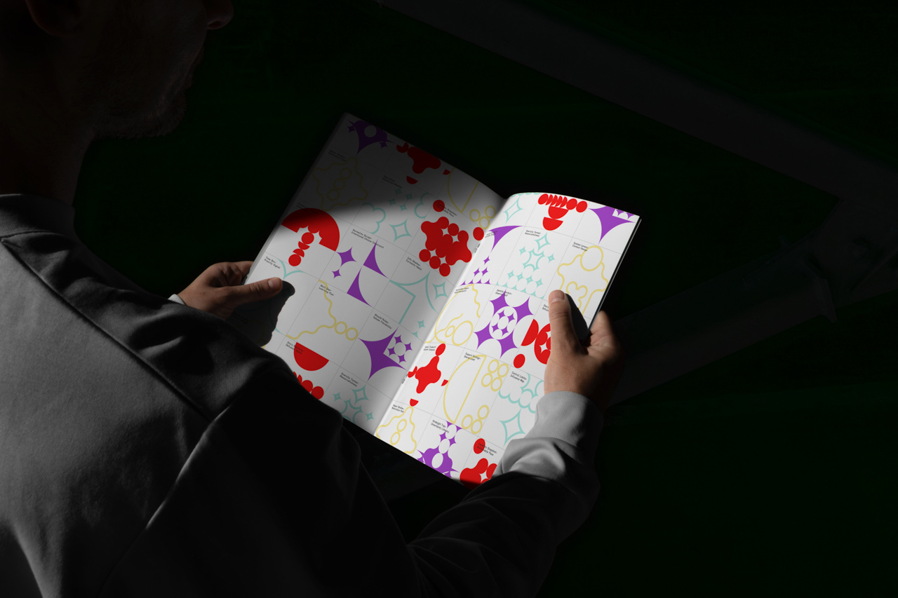 Person holding an open magazine featuring colorful abstract geometric illustrations in red, purple, yellow, and mint on both pages.
