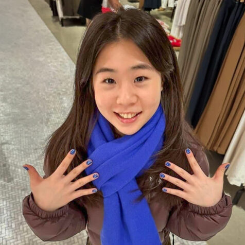 woman with long hair smiling and looking at camera. she is showing off her polka-dotted fingernails