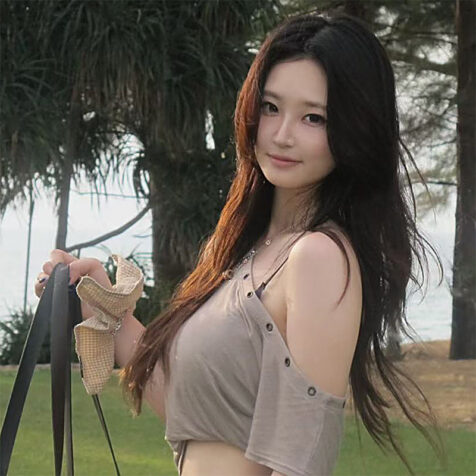 woman with long hair looking at camera, holding a purse, trees in background