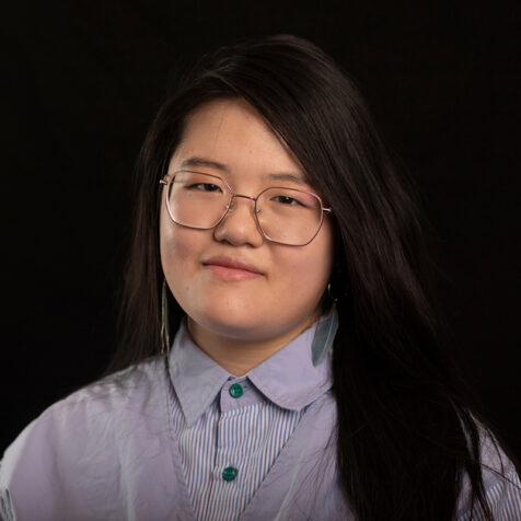 woman with glasses and long hair looking at the camera. black background