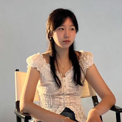 a woman with long hair sitting in a director chair looking off to the side.