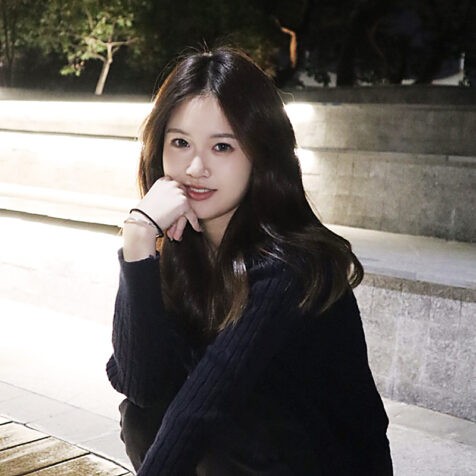 woman with long hair outside, looking at the camera, smiling.